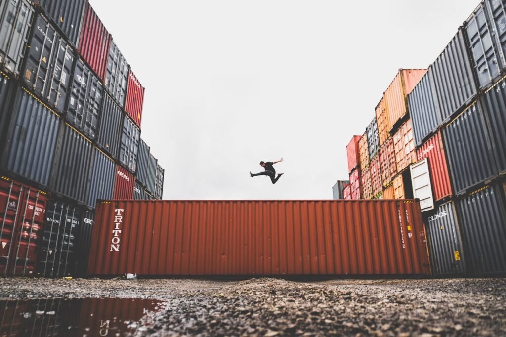About A person leaps dramatically above stacked shipping containers, showcasing freedom and industrial energy.